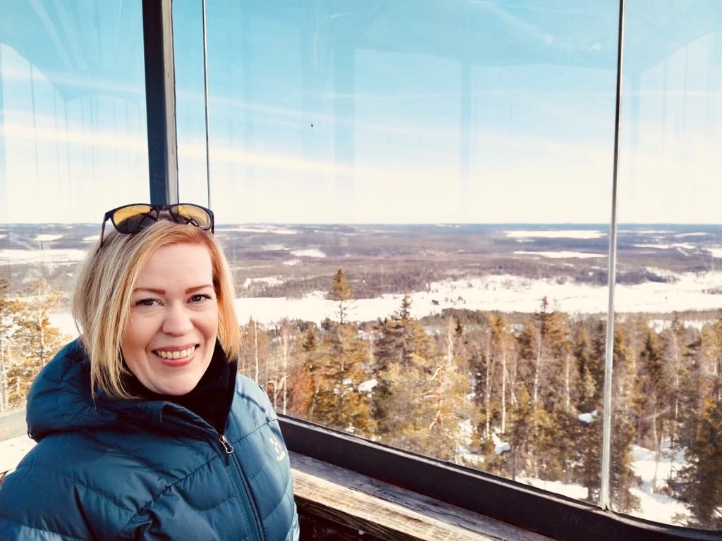 Vaaleahiuksinen nainen, jolla on aurinkolasit pään päällä. Taustalla luontomaisema,