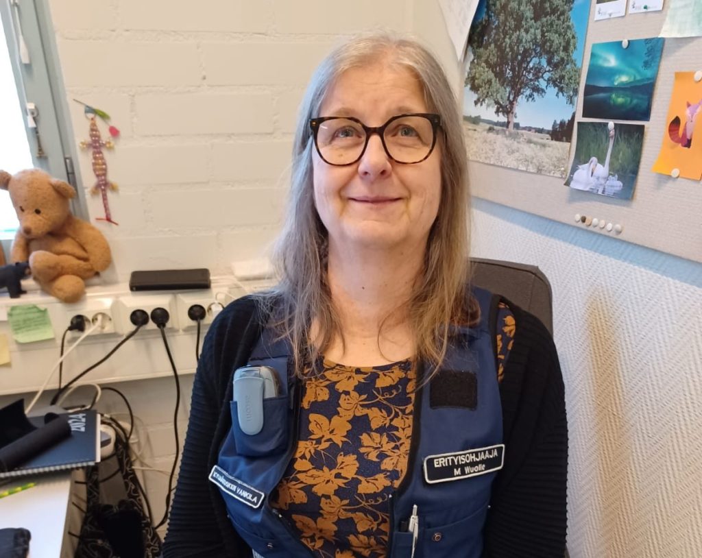 Kuvassa istuva nainen, jolla on yllään sininen liivi, jossa nimilapussa lukee Erityisohjaaja.