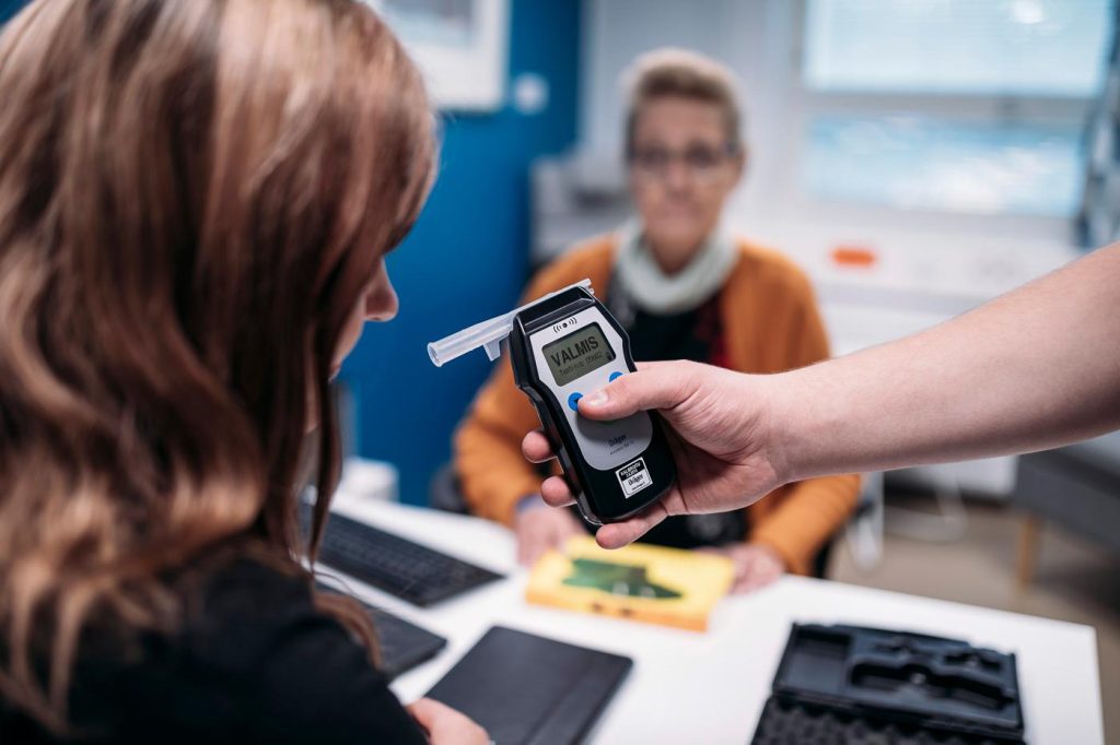 Nainen puhallutetaan digitaalisella alkometrilla. Toinen nainen valvoo.