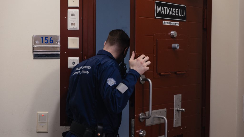 Rikosseuraamuslaitoksen työasuun pukeutunut mies pitää matkasellin oven kahvasta kiinni ja kurkkaa selliin.