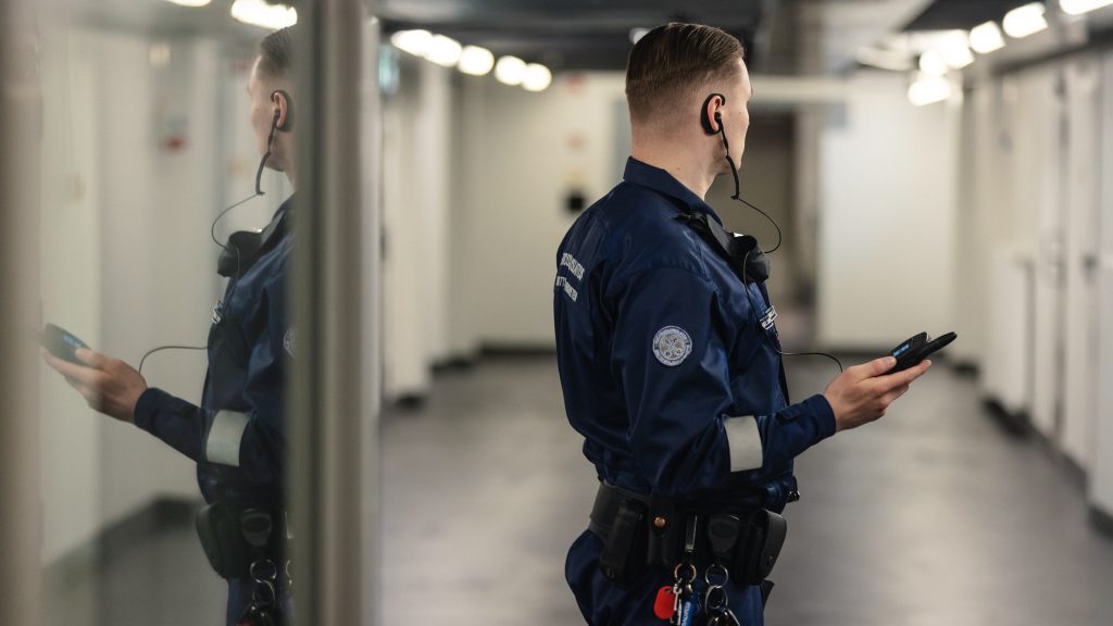 Vartija pitää viranomaispuhelinta kädessä vankilan sellikäytävällä.