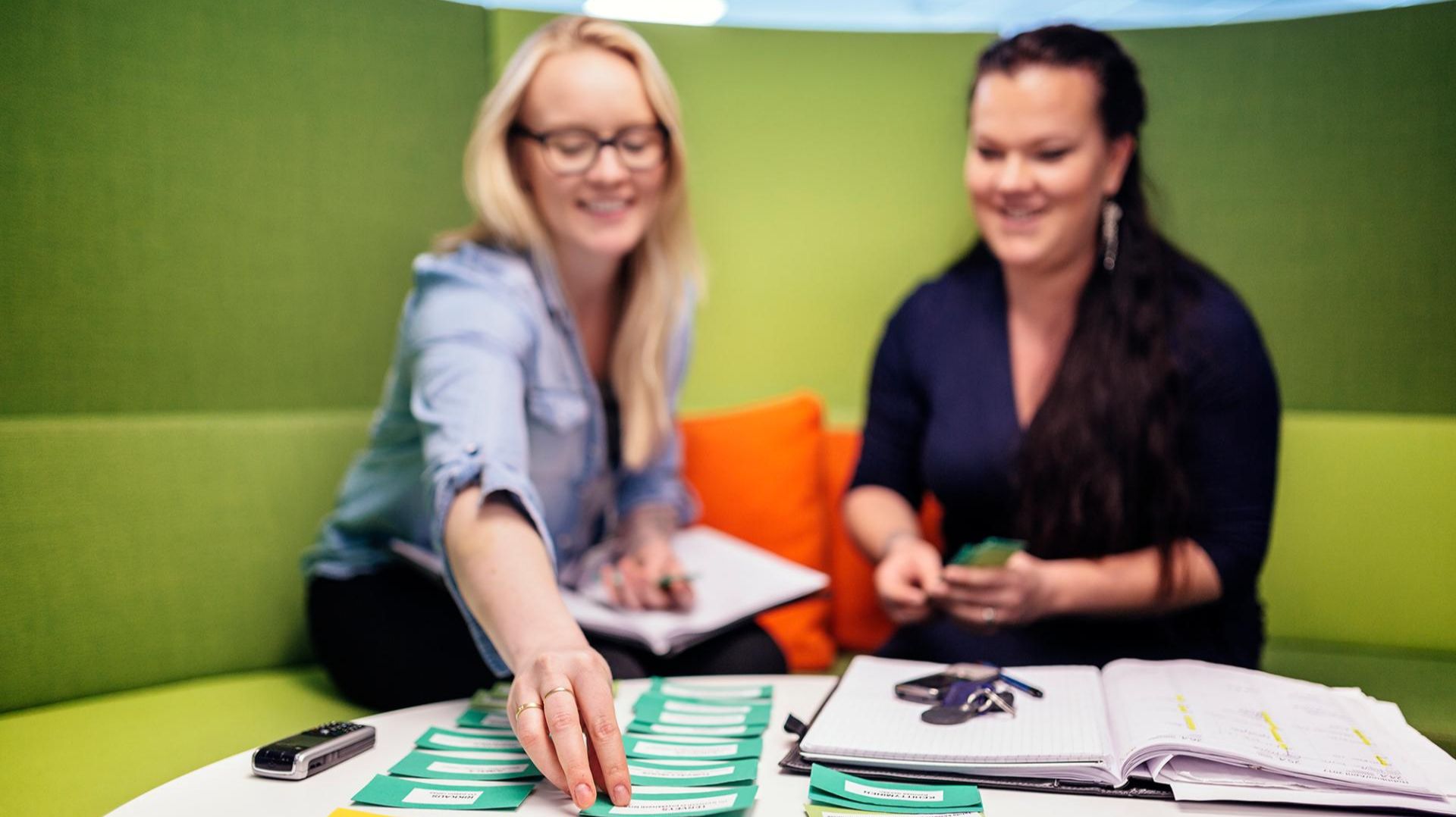 Two people sit at a table covered with colourful pieces of paper.