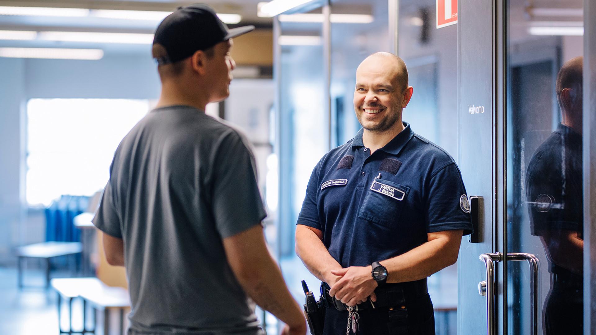 Två personer diskuterar. Den som står med ansikte mot kameran bär en uniform där det står väktare på bröstet. Två personer diskuterar. Den som står med ansikte mot kameran bär en uniform där det står väktare på bröstet.