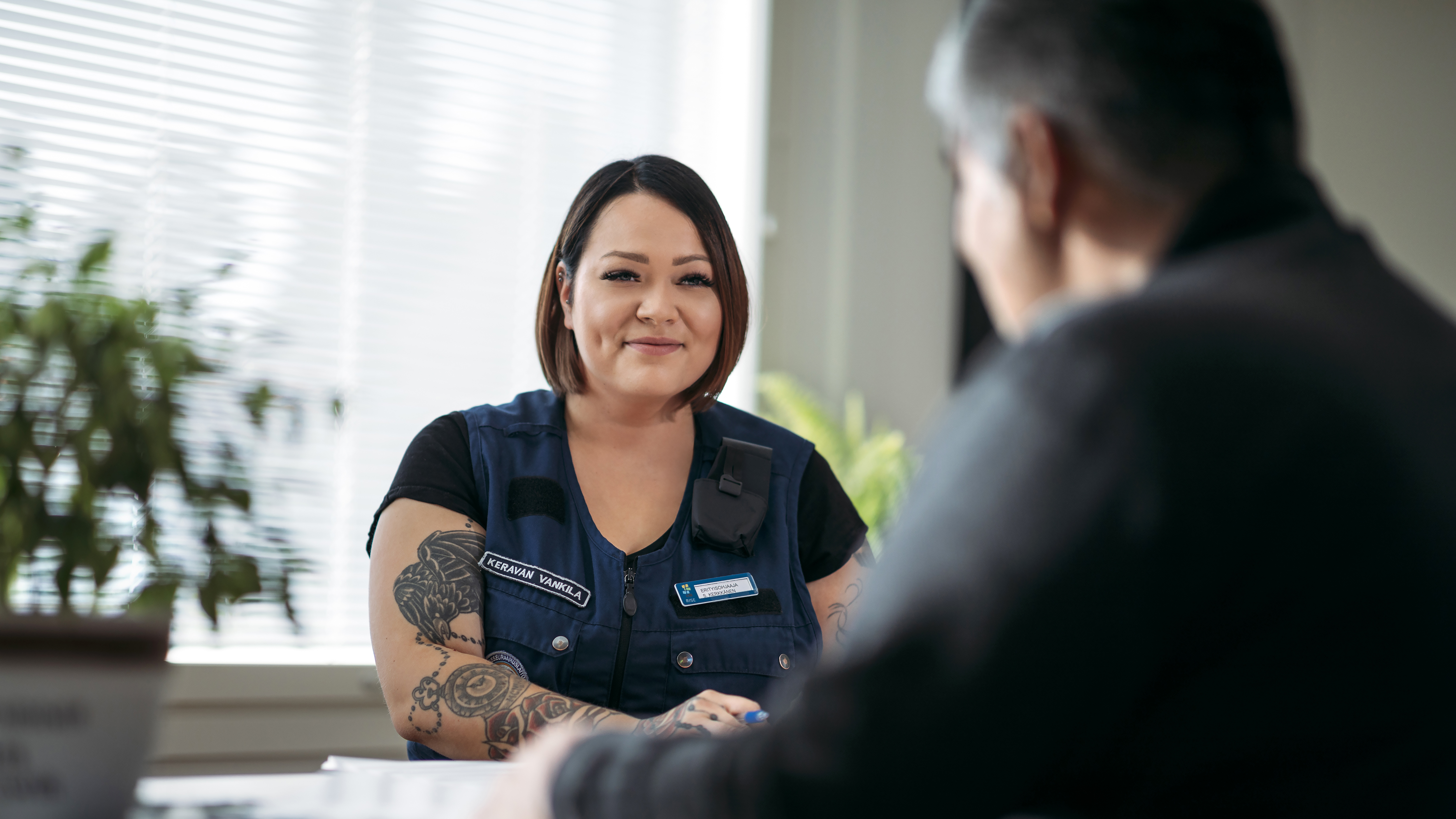 A woman, who wears a multi-pocket vest with the Prison and Probation Service logo, talks with a man, who is facing away from the camera.
