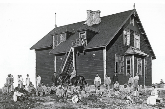 Vanha mustavalkoinen valokuva, jossa iso joukko ihmisiä oleskelee korkean asuinrakennuksen äärellä.
