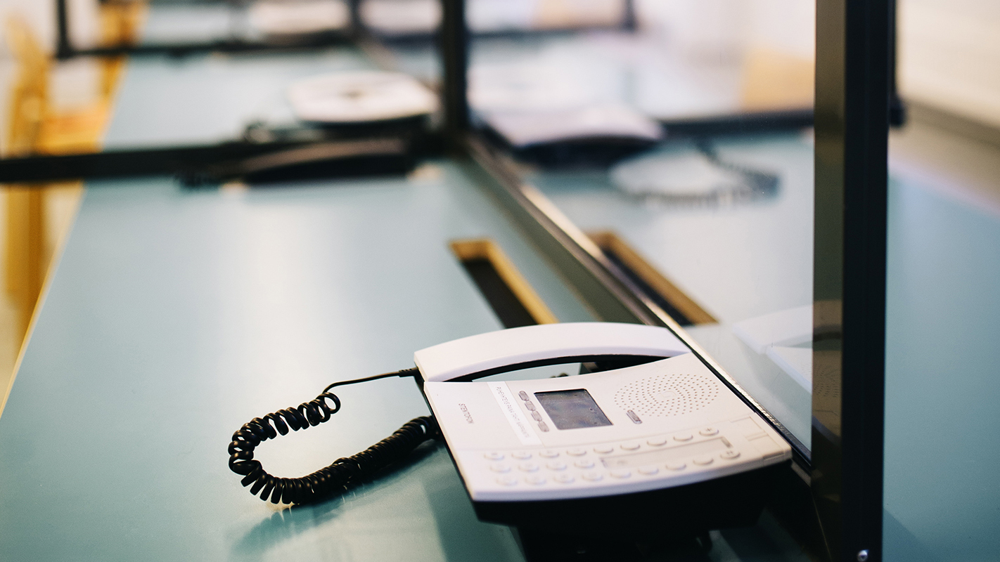 A white telephone is on a table. The table is divided into booths by glass screens.