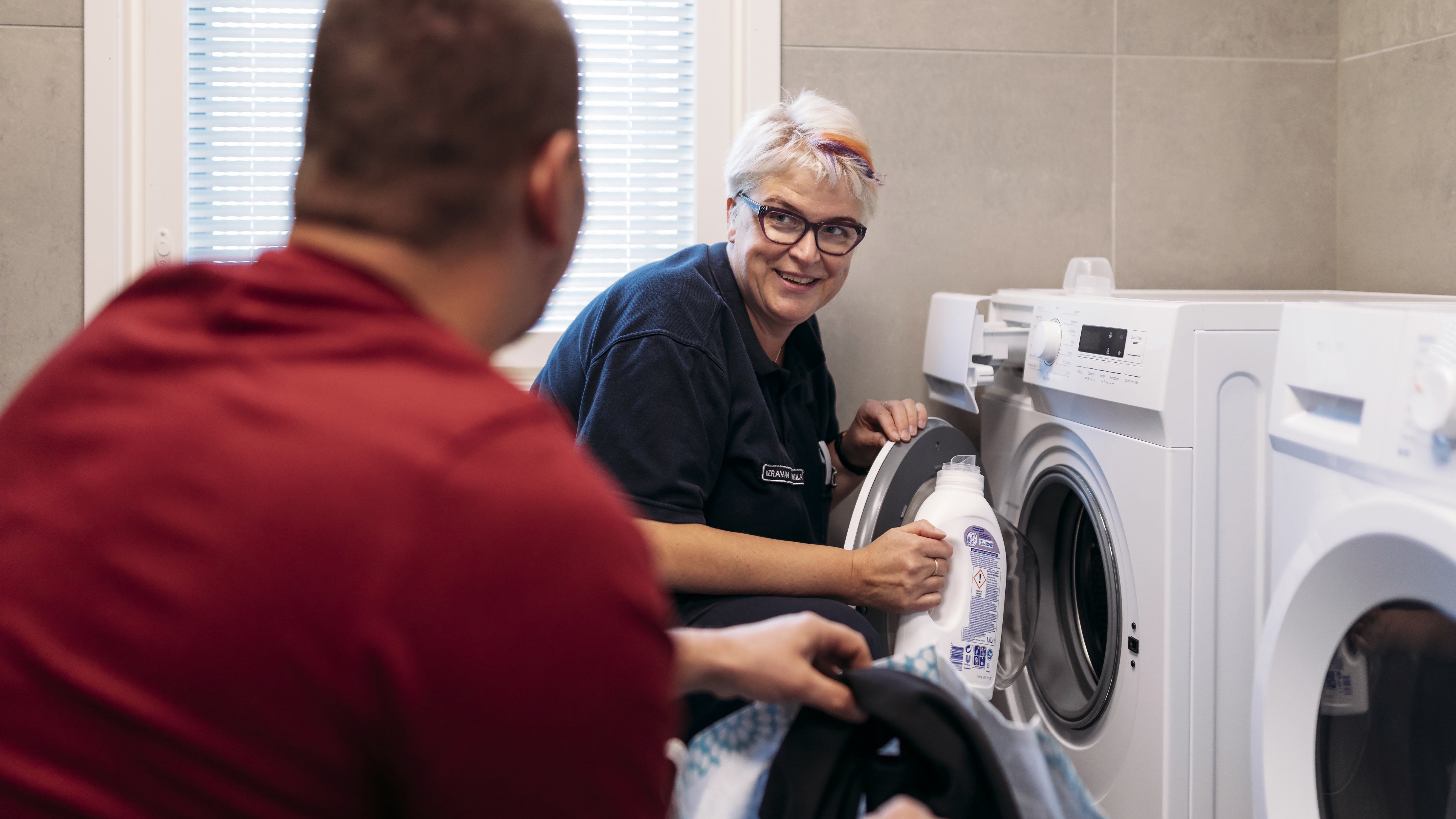 A man wearing a red shirt is doing the laundry with an official of the Prison and Probation Service.