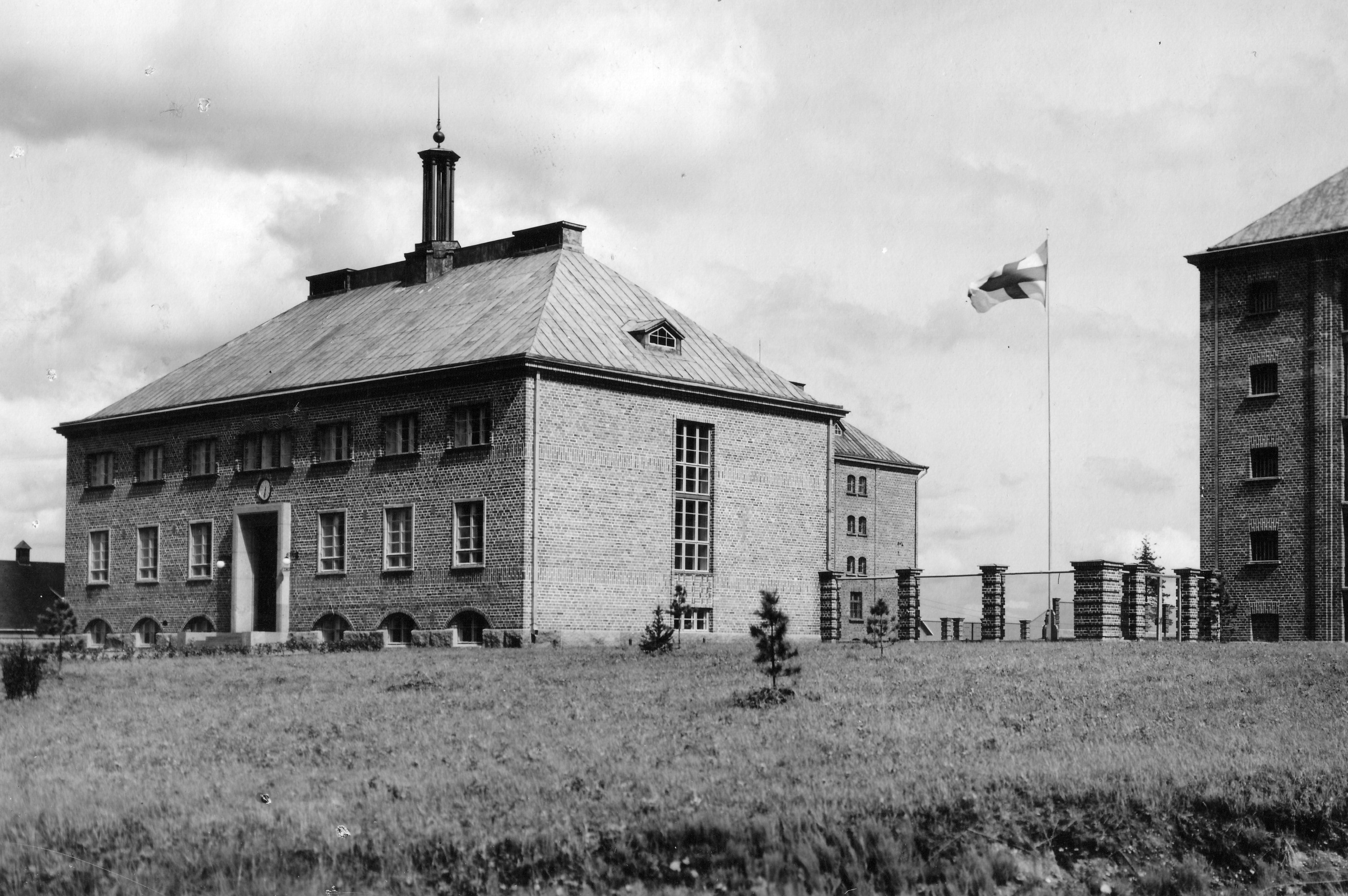 Mustavalkokuva, jossa on korkea, monikerroksinen tiilirakennus. Pihalla liehuu lippu.